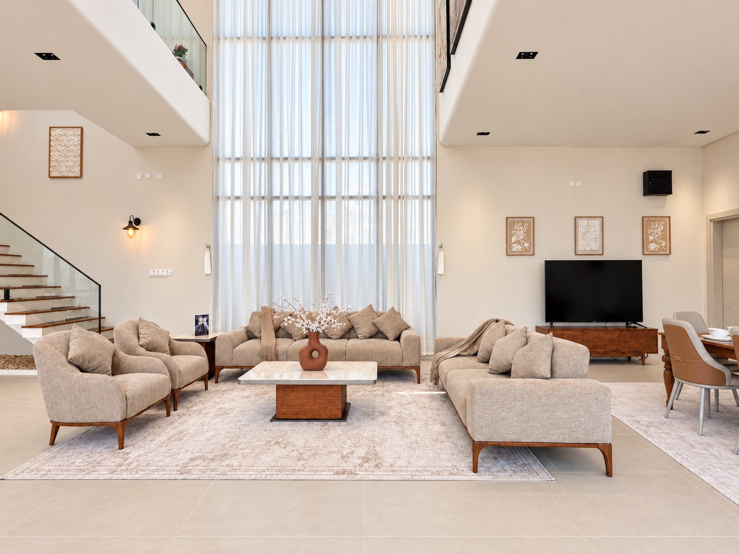 Kenaz double-height living room with beige sofas, tall curtains and a floating staircase